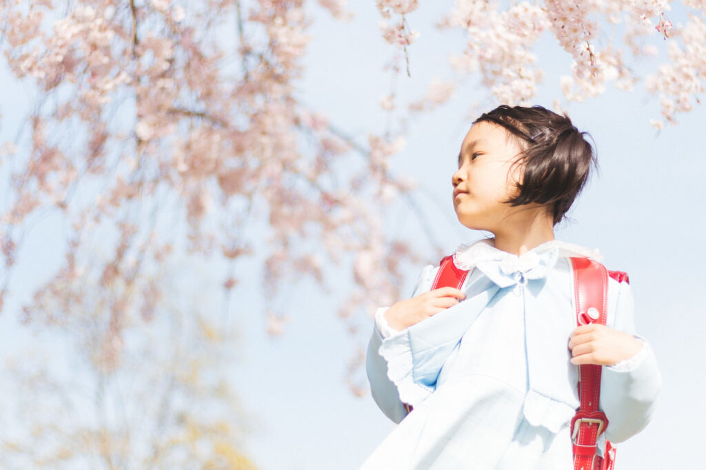 桜の花の下でランドセルを背負った小学生の女の子